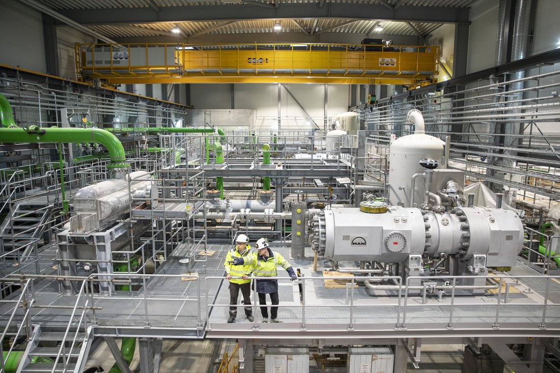 eine rieisige Wärmepumpenanlage mir zwei Männern in Warnwesten auf einem Eisensteg davor